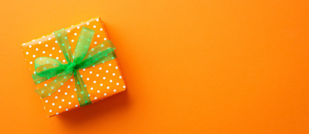 圣帕特里克节的概念。顶部视图照片的橙色礼盒在包装纸与波点图案和绿色丝带蝴蝶结孤立的橙色背景与复制空间图片下载