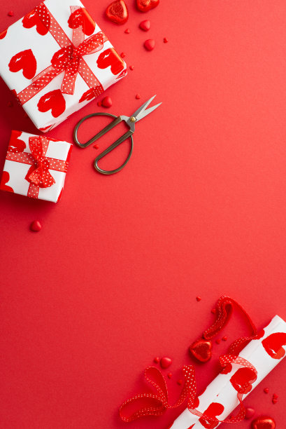 情人节的概念。俯视图垂直照片的礼盒剪刀包装纸卷丝带心形糖果和洒在孤立的红色背景与复制空间图片下载