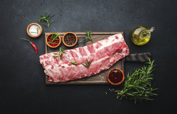 生猪肉排骨与迷迭香和香料在乡村木砧板上准备烹饪黑色厨房桌子背景，俯视图图片下载