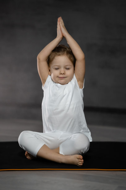 三岁的小女孩在一个黑暗的房间里，在灰色的背景上以莲花的姿势冥想图片下载