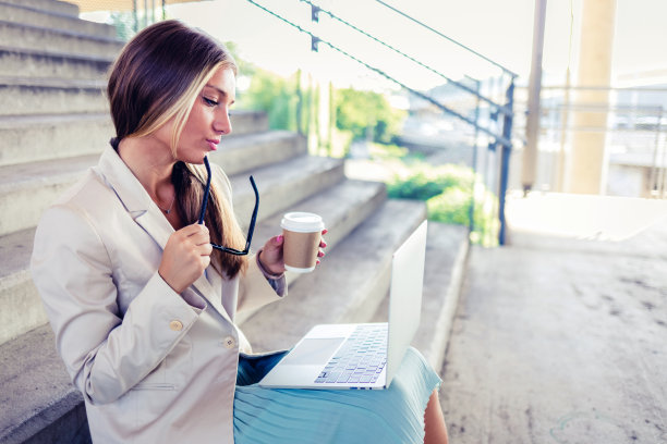 一个年轻的女商人白天在外面的楼梯上使用笔记本电脑。图片下载