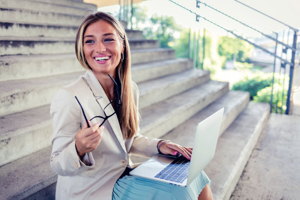 微笑的年轻非洲裔美国妇女工作在无线笔记本电脑，而坐在楼梯附近的公共公园。迷人的女性自由职业者享受远程工作的新鲜空气。图片下载