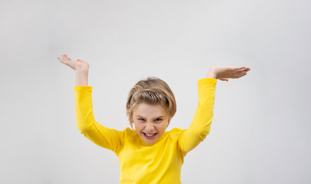 快乐的情感学校男孩快乐地挥舞着双手在白色的背景。金发孩子，长发，黄t恤，兴奋地挥舞着双手图片下载