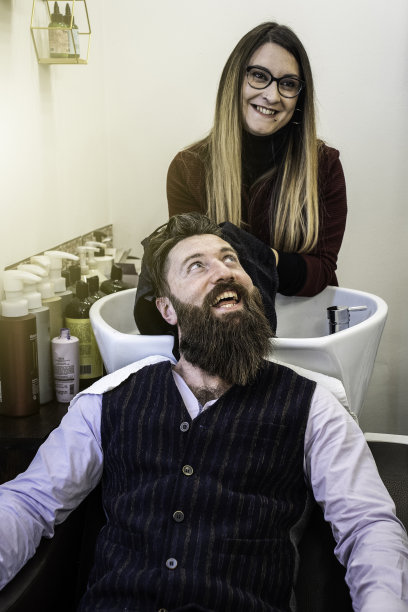 女理发师在洗脸盆冲洗后烘干潮人客户的头发-微笑的潮人在理发店沙龙得到胡子和头发剪-理发店的概念图片下载