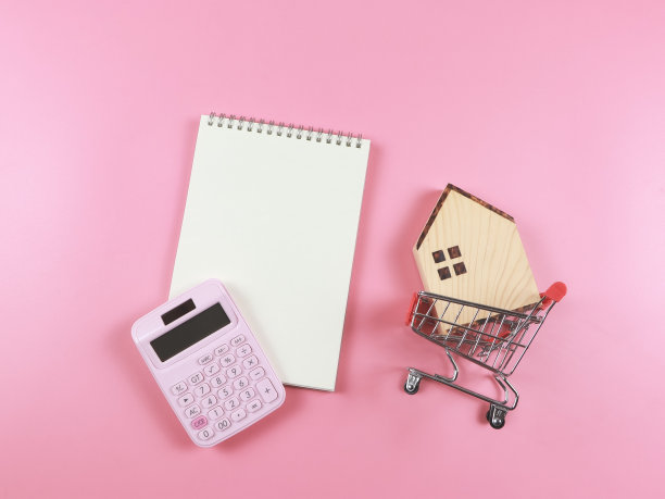 平面布局的木屋模型购物车，粉红色计算器，空白页笔记本上的粉红色背景与复制空间，购房概念。图片下载