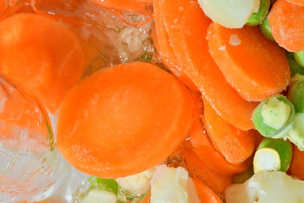 近景的汤蔬菜与胡萝卜，豌豆，花椰菜和玉米在水的背景。冷冻蔬菜汤的口感。把水倒进冷冻蔬菜汤里。平面设计。水平的形象图片下载