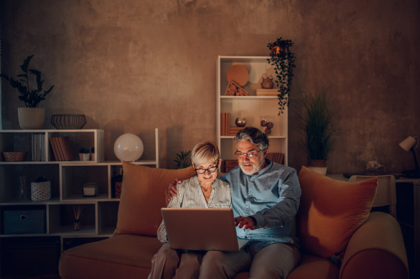 老夫妇坐在家里的沙发上使用笔记本电脑图片下载