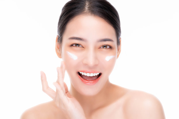美丽的亚洲女性将保湿霜涂在美丽的脸上快乐的年轻亚洲女性拥有美丽的面部皮肤迷人的女孩看着相机，微笑的脸孤立在白色的背景上图片下载
