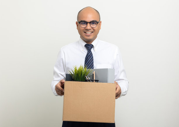 员工第一天上班。快乐的商人与纸箱个人物品获得新工作。年轻人开始在孤立的白色背景上工作。图片下载