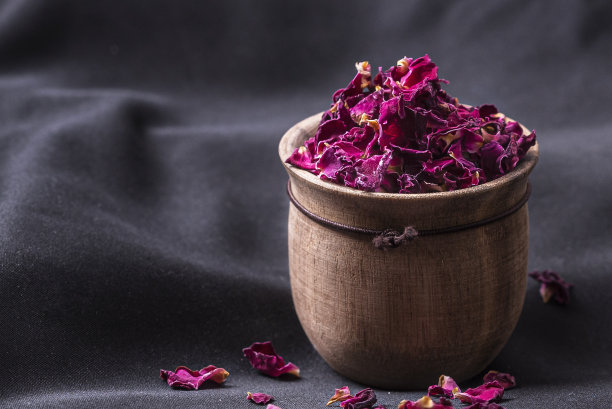 特写镜头，干燥的玫瑰花瓣在一个木壶上的黑色织物图片下载