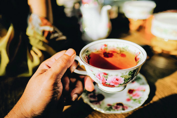 特写镜头是一只手拿着一个白色装饰的茶杯，放在木制的桌子背景上图片下载