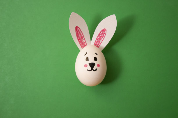 儿童复活节彩蛋玩具。鸡蛋配兔子耳朵，绿色背景图片下载