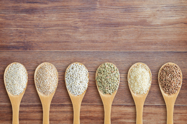 谷物放在木勺上排成一排。棕色木质背景。图片下载