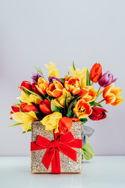 庆典概念-金色礼盒，红色丝绒丝带和郁金香花束。垂直卡片模型。妇女节，三月八，母亲节，生日问候。有选择性的重点。本空间图片下载