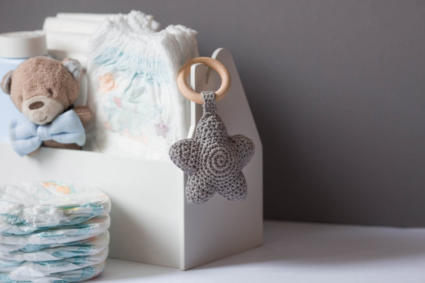 木制玩具、戴领结的熊、一堆尿布、没有标签的奶瓶和婴儿用品放在换尿布的桌子上。文本空格。图片下载