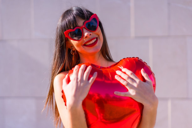 美丽的照片，一个白人女孩抱着心形气球在情人节戴着太阳镜图片下载