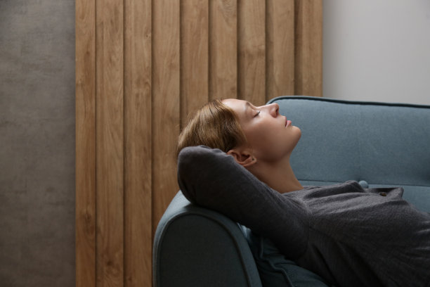 年轻漂亮的女人在沙发上放松的侧面视图，女人靠在舒适的沙发上图片下载