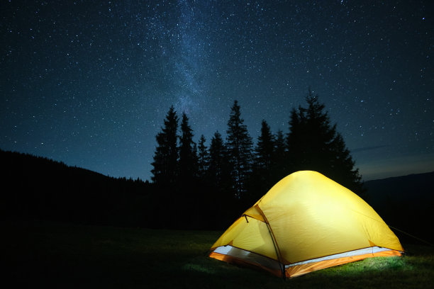 明亮照明的旅游帐篷在夜空下闪烁的星星在黑暗的山露营地发光。积极的生活方式概念。图片下载