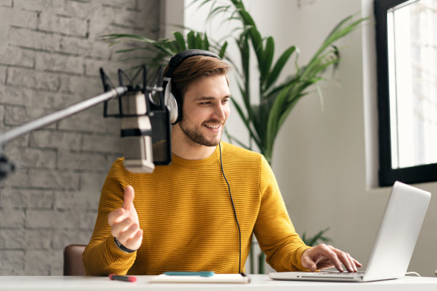 男子博主微笑着在演播室用耳机、笔记本电脑和耳机直播他的音频播客图片下载