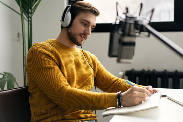 男子博主微笑着在演播室用耳机、笔记本电脑和耳机直播他的音频播客图片下载