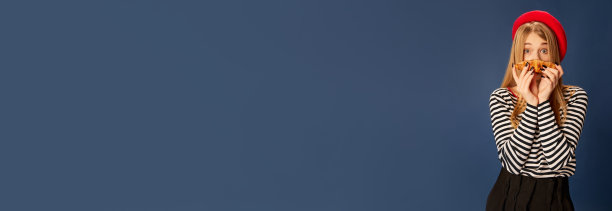 美丽的年轻女孩在红色贝雷帽摆造型与新鲜出炉的羊角面包在蓝色工作室背景的肖像。时尚、美丽和生活方式的概念图片下载
