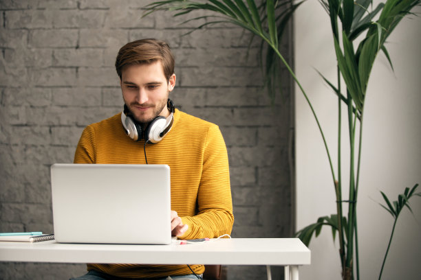 穿着随意的年轻设计师戴着耳机在办公室里用笔记本电脑工作图片下载