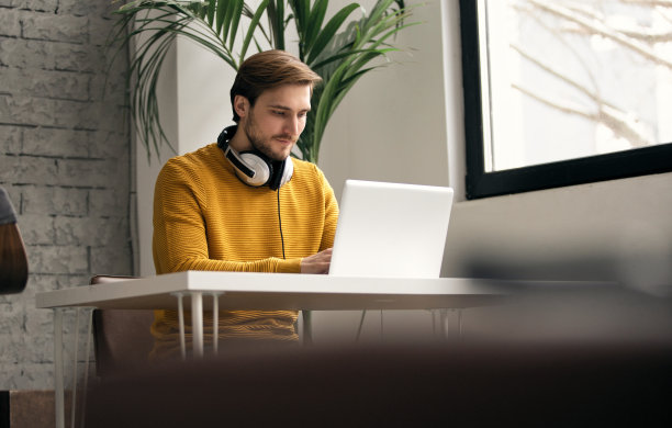 穿着随意的年轻设计师戴着耳机在办公室里用笔记本电脑工作图片下载