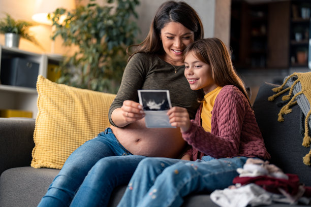 微笑的母亲和女儿在家里一起看超声波婴儿的照片图片下载