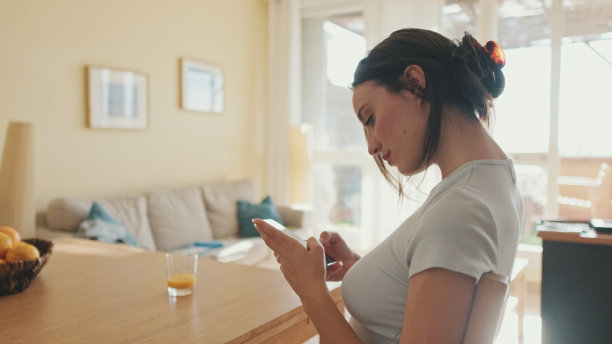 微笑的年轻女子坐在厨房里，用手机浏览照片图片下载