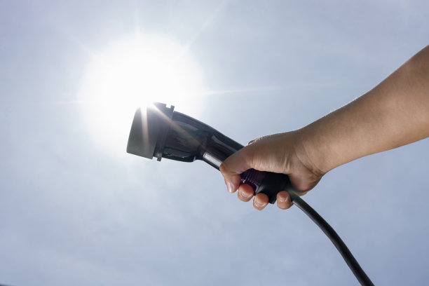 下面的视图图像手握渐进式电动汽车充电器与天空背景。图片下载