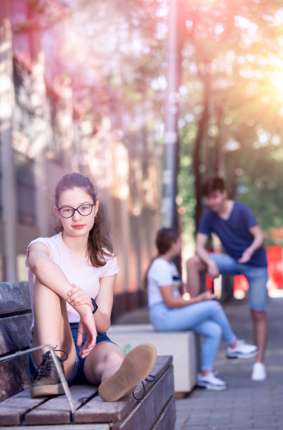 十几岁的女孩戴着眼镜坐在城市街道的长凳上图片下载