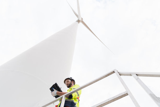 男性工程师，负责风力发电机的计划检查和维护工作。男性工程师使用平板电脑控制或监测风力涡轮机农场的风力涡轮机系统图片下载