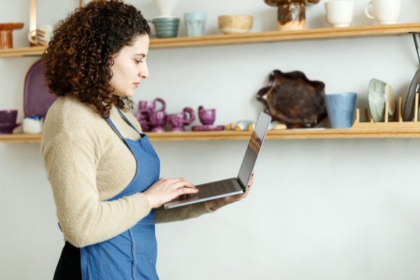 年轻的女企业家，企业主工作在家里办公室与她的粘土陶瓷产品。网上销售业务工作，持有电脑图片下载