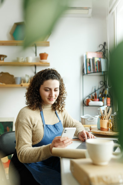 女陶艺家正在用智能手机看短信。有创意的女商人管理着一家收藏陶瓷产品的商店。年轻的企业家经营着一家成功的小公司图片下载
