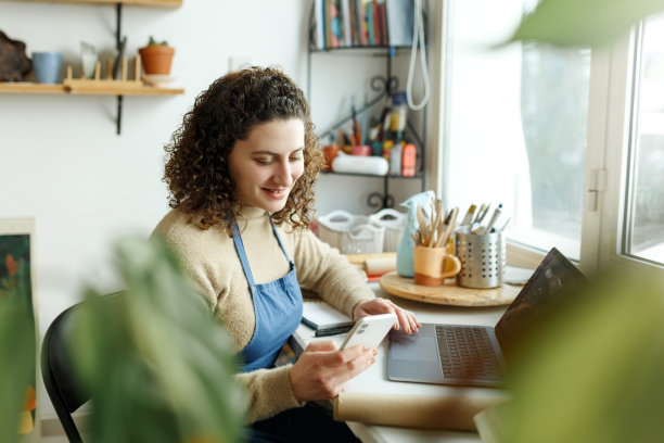 女陶艺家正在用智能手机看短信。有创意的女商人管理着一家收藏陶瓷产品的商店。年轻的企业家经营着一家成功的小公司图片下载