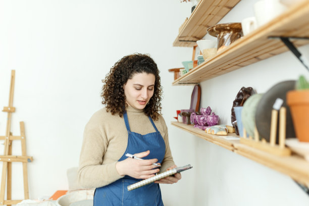 快乐的年轻陶艺家一边看一边沉思。有创意的女商人经营一家手工陶瓷产品商店。女性企业家经营着一家成功的小企业图片下载