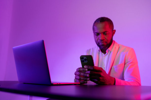 一位面带微笑的商人拿着笔记本电脑正在打电话。晚上在电话上工作图片下载