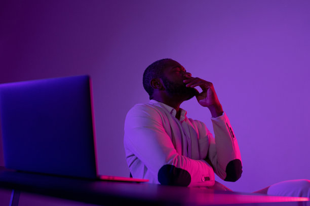 照片中穿着白色西装的男子在夜间办公室的电脑旁思考新的网络安全项目图片下载