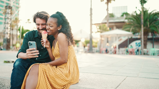 快乐的男人和微笑的女人在智能手机上观看视频的肖像。在城市背景下，快乐的年轻跨种族夫妇在手机上浏览照片的特写图片下载