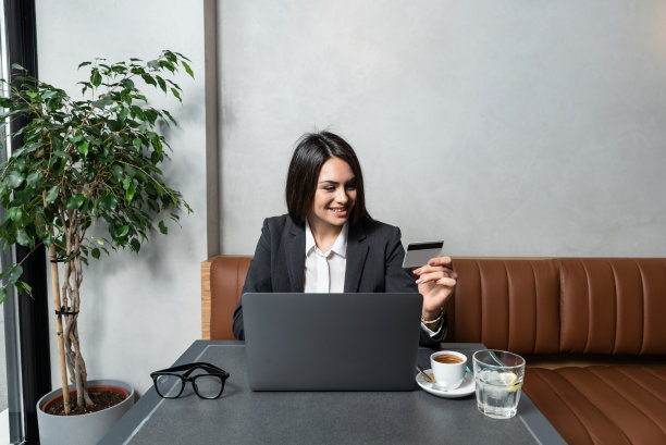一名年轻的女商人在一家自助餐厅休息时喝着咖啡，用信用卡在网上订购她在网上商店网站上发现的新化妆品和衣柜。图片下载
