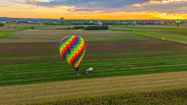 鸟瞰图热气球降落在农田玉米田旁边，汽车带着拖车停在气球旁边，热气球在远处图片下载