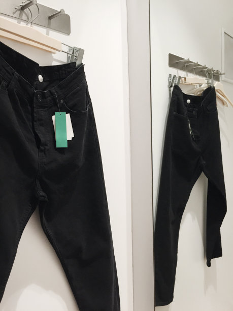 在服装店试衣间的衣架上挂着黑色牛仔裤，上面有空白的价签图片下载