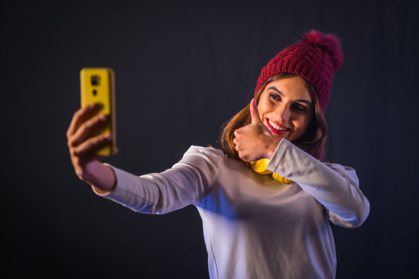 年轻的黑发白种人，戴着黄色耳机和羊毛帽子，用手机自拍图片下载