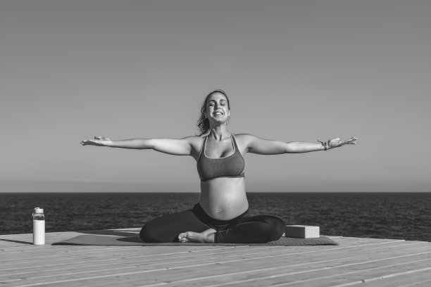 年轻的孕妇做瑜伽会议旁边的海-冥想和孕产概念-黑白编辑图片下载