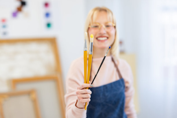 年轻的画家拿着画笔站在画室里图片下载