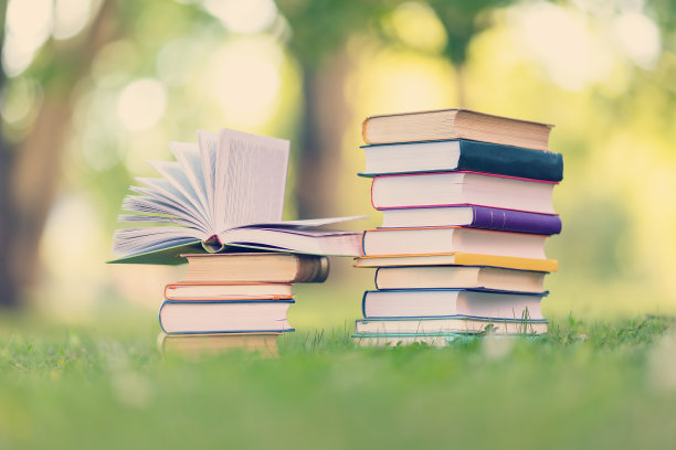 一摞书立在户外的绿色草地上。图片下载