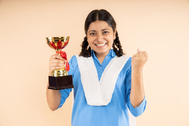 快乐的农村印度学生女学生穿着蓝色政府校服手持胜利奖杯孤立在米色背景，获胜者，工作室拍摄，特写，教育概念。图片下载