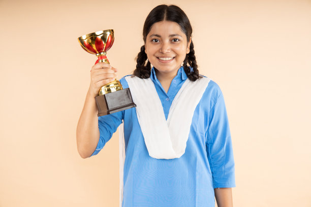 快乐的农村印度学生女学生穿着蓝色政府校服手持胜利奖杯孤立在米色背景，获胜者，工作室拍摄，特写，教育概念。图片下载