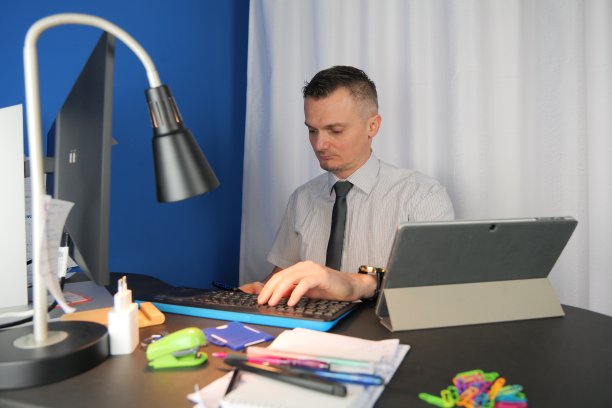 一位身穿白色衬衫、系着棕色领带的中年白人男子坐在办公室或家庭办公桌前图片下载