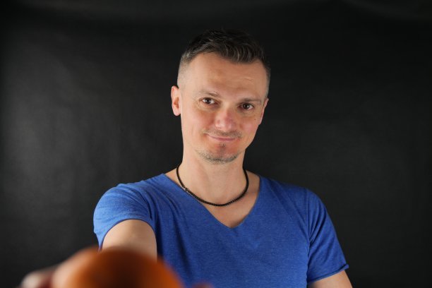 一名身穿蓝色t恤的白人青年手里拿着橘子，正在拍摄照片。图片下载